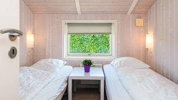 A small room with two beds, a window with a view of greenery, a small table with a plant, and a door with a lock.