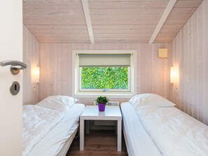 A small room with two beds, a window with a view of greenery, a small table with a plant, and a door with a lock.
