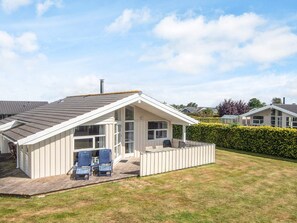 A single-story house with a sloped roof, a covered patio with two chairs, and a well-maintained lawn. - Pleasing Holiday Home in Haderslev near Sea (Haderslev)