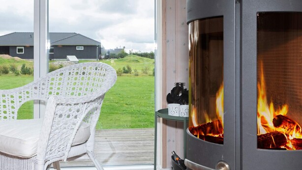 A modern room with a large glass door leading to a grassy outdoor area, a white wicker chair, and a wood-burning stove.