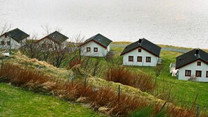 File d'habitatges blancs amb sostres foscos, ubicats en un turó verd que domina una extensa massa d'aigua.