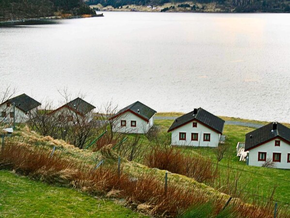 A row of white houses with dark roofs, situated on a grassy hill overlooking a large body of water.