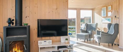 A modern living room with a wood-burning stove, a flat-screen TV, and a seating area with two grey armchairs.
