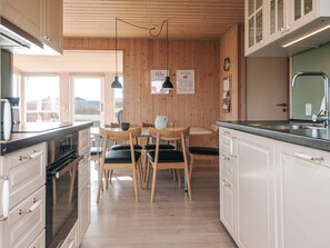 A modern kitchen with wooden cabinets, a dining area with a table and chairs, and a view of the outside. - Spacious Holiday Home in Hejls near Sea (Hejls)