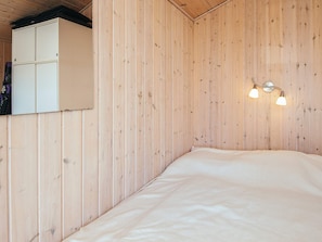 A room with wooden panel walls, a bed with white bedding, and a wall-mounted light fixture.