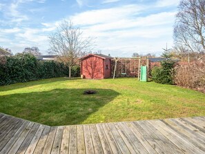 Un jardin avec une terrasse en bois, une balançoire et un abri de jardin rouge.