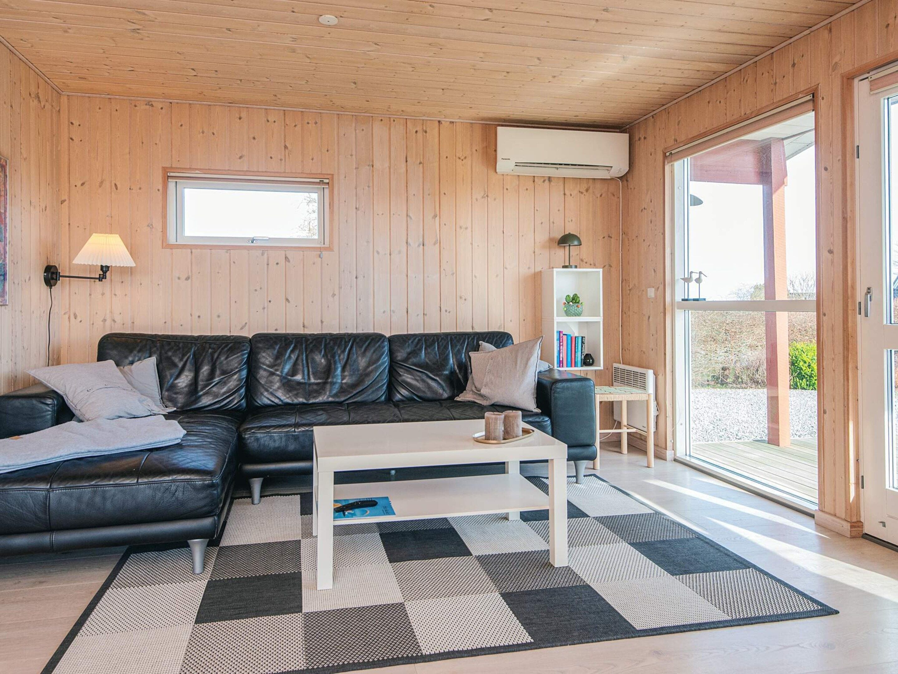 A cozy living room with a black leather sofa, a white coffee table, and a checkered rug.