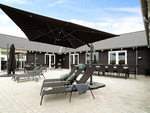 An outdoor patio with lounge chairs and a large umbrella, a grill, and a building with a tiled roof. - 30 Person Holiday Home in Bogense (Bogense)
