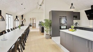 A modern kitchen with a long dining table, dark cabinets, and pendant lighting. - 30 Person Holiday Home in Bogense (Bogense)