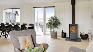 A modern living room with a fireplace, dining area, and a large window. - 30 Person Holiday Home in Bogense (Bogense)