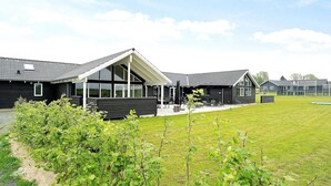 A modern building with a large glass facade, a covered outdoor seating area, and a grassy lawn. - 30 Person Holiday Home in Bogense (Bogense)