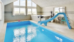 An indoor swimming pool with a blue slide, a hot tub, and large windows offering a view. - 30 Person Holiday Home in Bogense (Bogense)