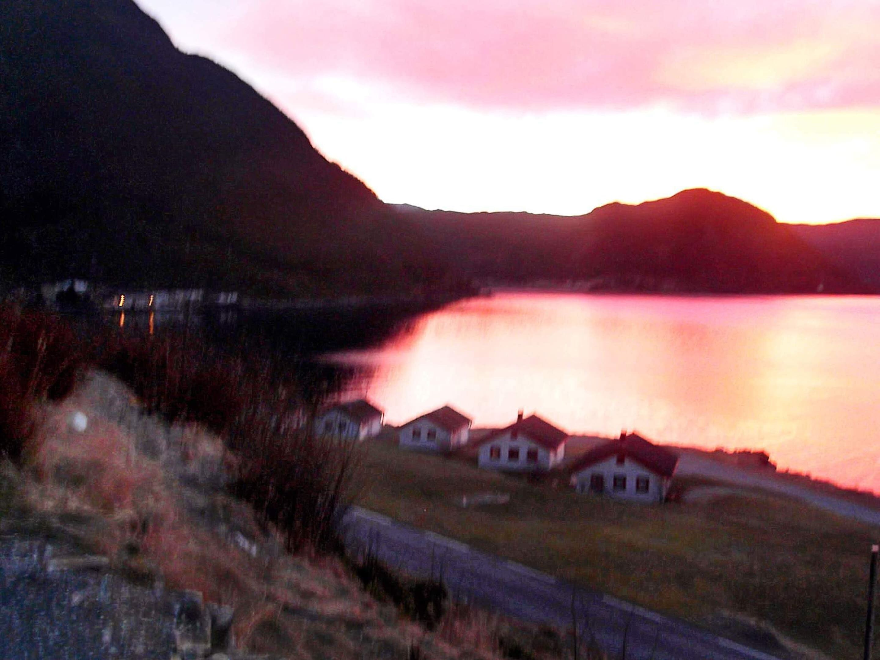 A view of a lake with houses in the foreground and a mountain in the background.