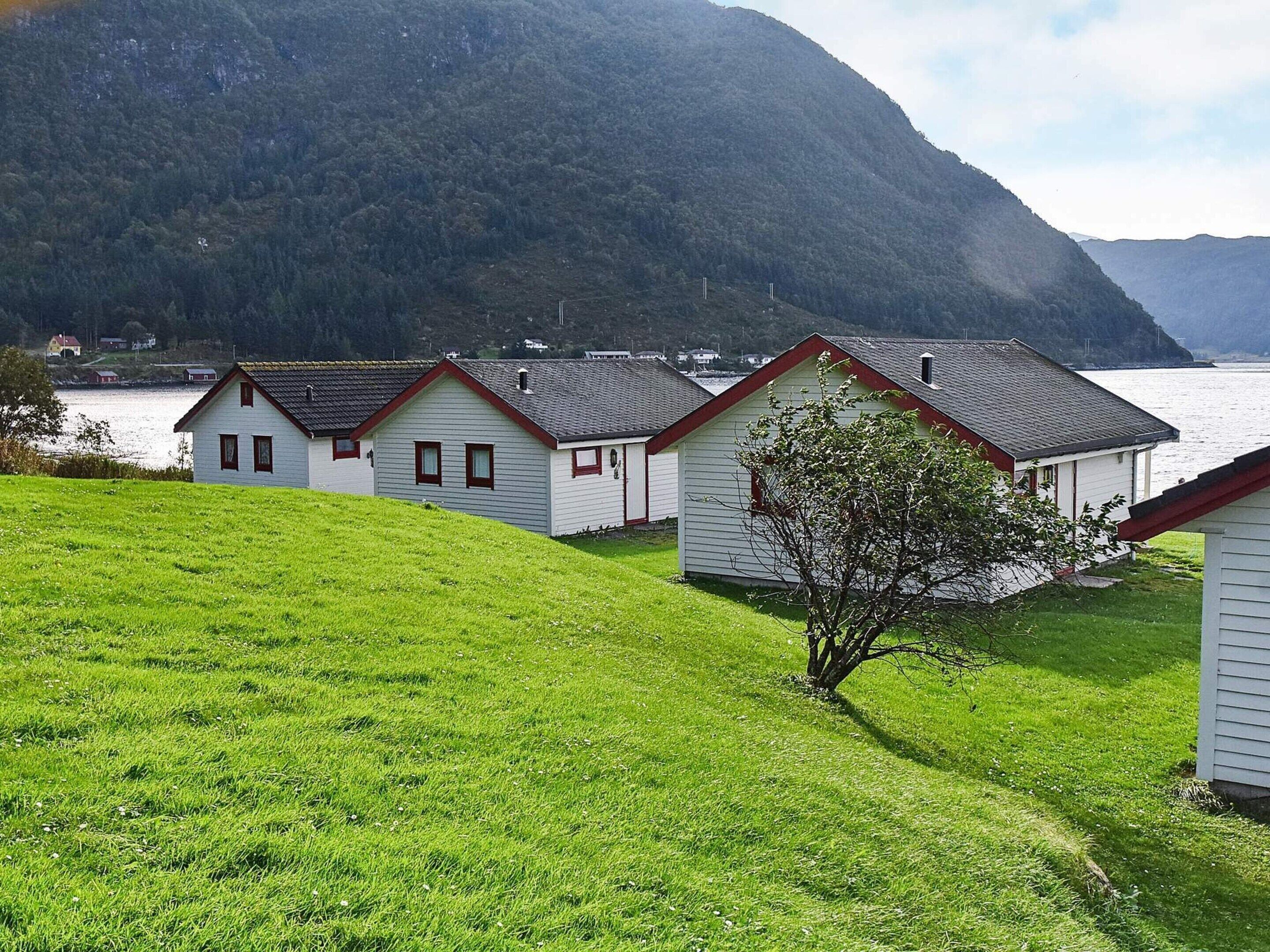 Une rangée de cabanes blanches aux bordures rouges, se dressant sur fond de lac et de montagnes.