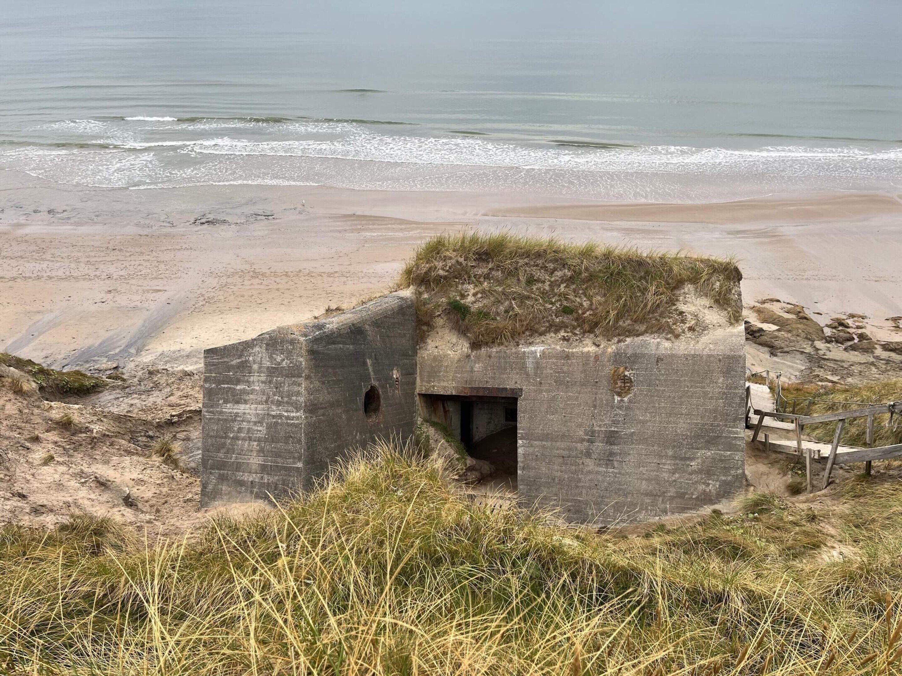 Une construction côtière dotée d’une petite entrée, entourée de plage et d’herbe.
