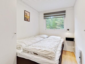 A small, single-bed room with a window, a bedside table, and a radiator.