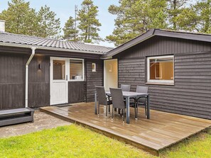 A small, dark wooden cabin with a deck and outdoor seating area.