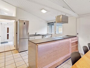 A modern kitchen with a stainless steel refrigerator, a sink, and a large island with a perforated design.