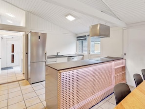 A modern kitchen with a stainless steel refrigerator, a sink, and a large island with a perforated design.