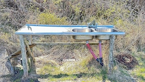 Une table de camping portable dotée de deux éviers en métal et d’un tuyau d’arrosage.