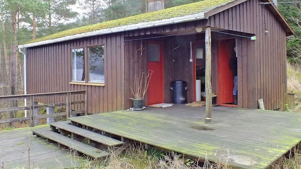 Une cabane en bois avec une véranda, une porte rouge et une cheminée.
