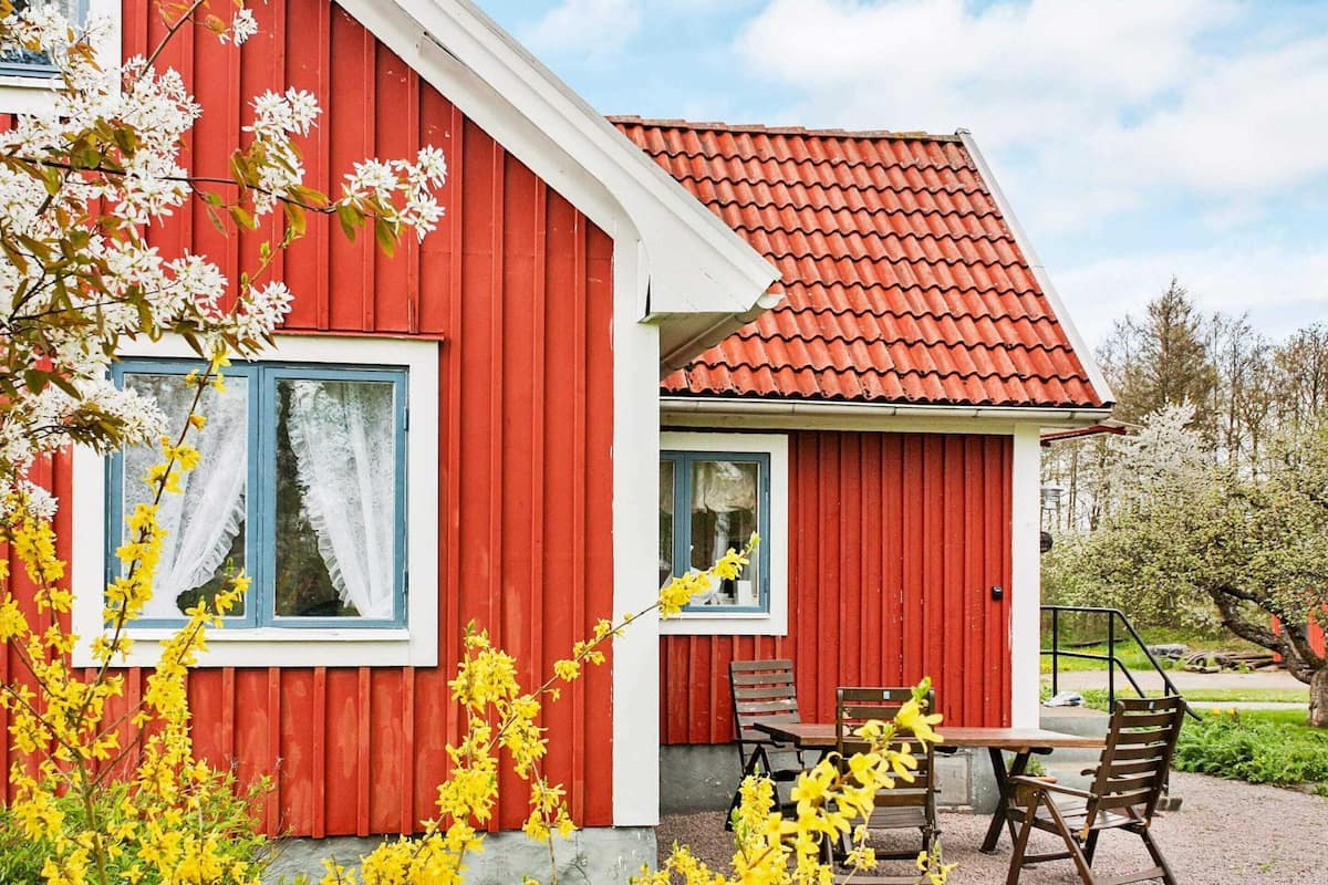 A red building with a tiled roof, a window with white curtains, and a small patio with a table and chairs.