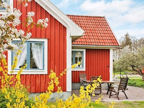 A red building with a tiled roof, a window with white curtains, and a small patio with a table and chairs.