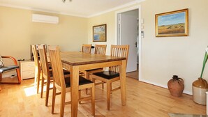 A dining area with a wooden table and chairs, a white door, and two framed pictures on the wall.