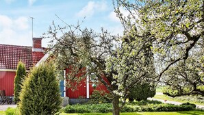 Ein gepflegter Garten mit einem roten Gebäude, einer ordentlich geschnittenen Hecke und blauem Himmel.