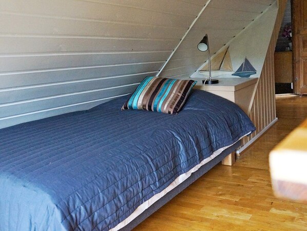 A single bed with a blue quilt, a striped pillow, and a small bedside table with a lamp. - Holiday Home in Söderåkra (Soderakra)