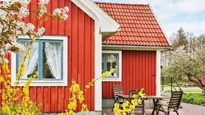Ein rotes Gebäude mit einem Ziegeldach, einem Fenster mit weißen Vorhängen und einer kleinen Terrasse mit Tisch und Stühlen.