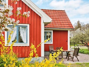 A red building with a tiled roof, a window with white curtains, and a small outdoor seating area with wooden furniture. - Holiday Home in Söderåkra (Soderakra)