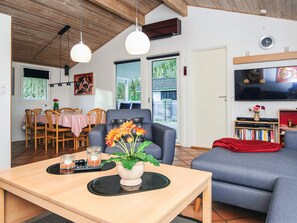 Una sala de estar con comedor, un sofá gris, un televisor y una estantería.