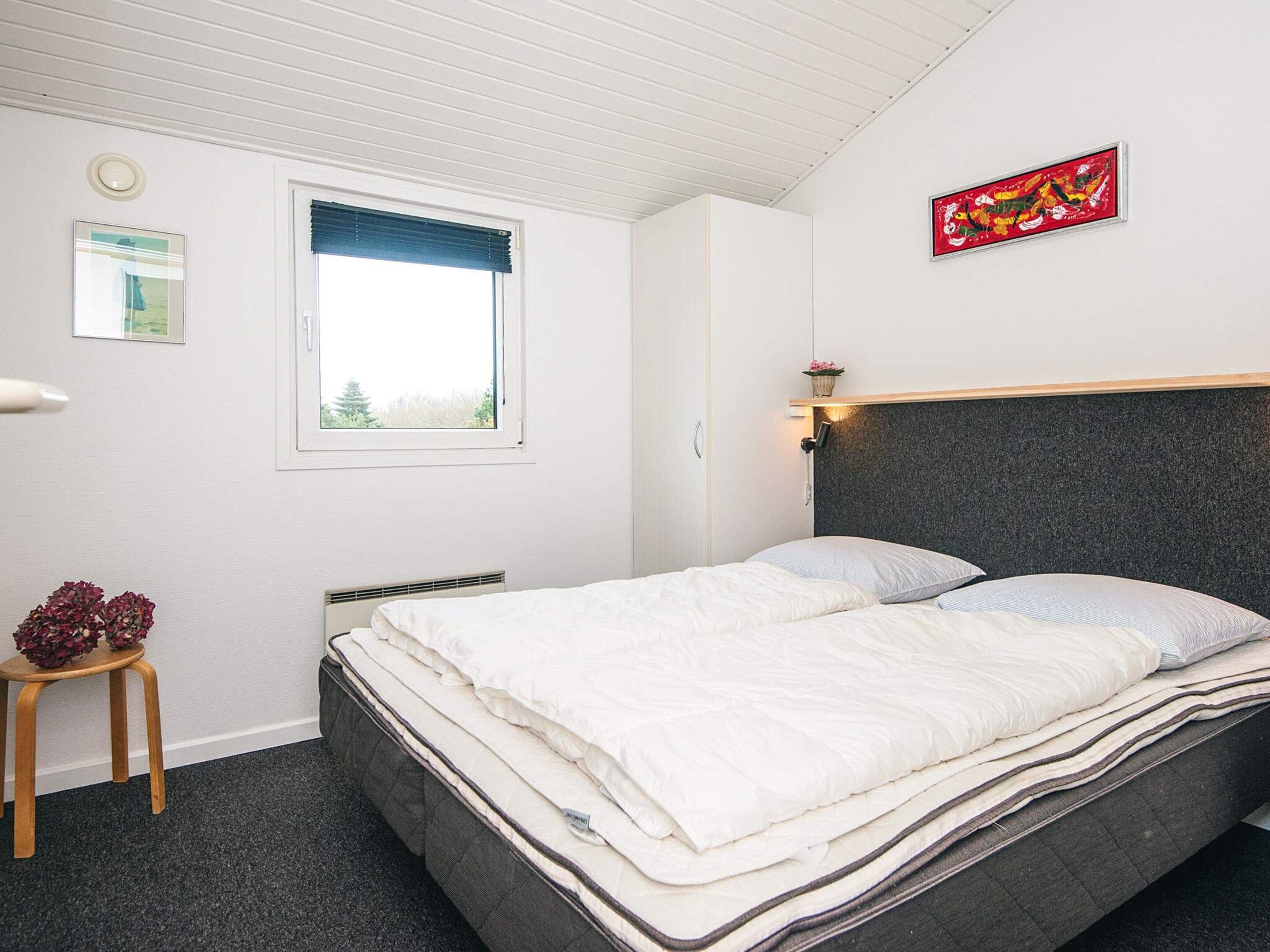 Ein Schlafzimmer mit einem Bett, einem Fenster, einer Wandleuchte und einem gerahmten Bild.