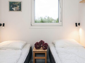 Una habitación con dos camas, una ventana, un cuadro en la pared y una pequeña mesa de madera con flores.