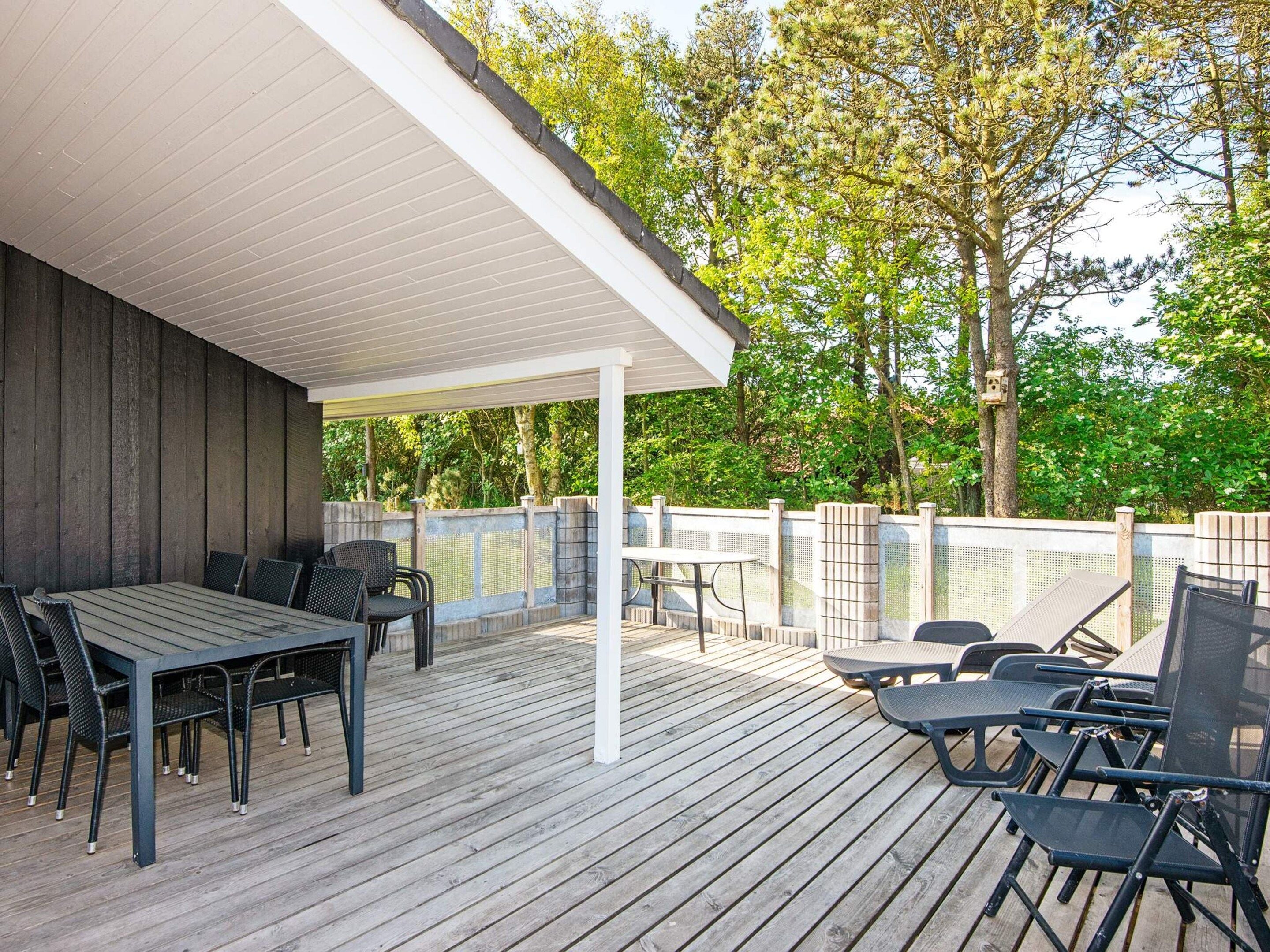 Eine Terrasse im Freien mit Tisch und Stühlen, umgeben von einem Holzzaun und Bäumen.