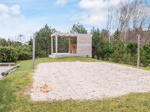 Eine Holzblockhütte mit überdachter Veranda, umgeben von Sand und dichtem Grün.