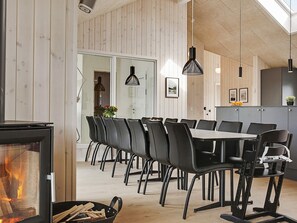 A modern dining area with a long table and chairs, a fireplace, and wooden walls. - 5 Star Holiday Home in Bogense (Bogense)