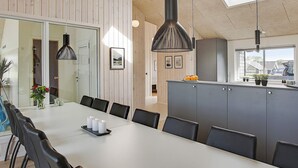 Moderni ruokailutila, jossa on pitkä pöytä, mustat tuolit ja riippuvalaisimet.