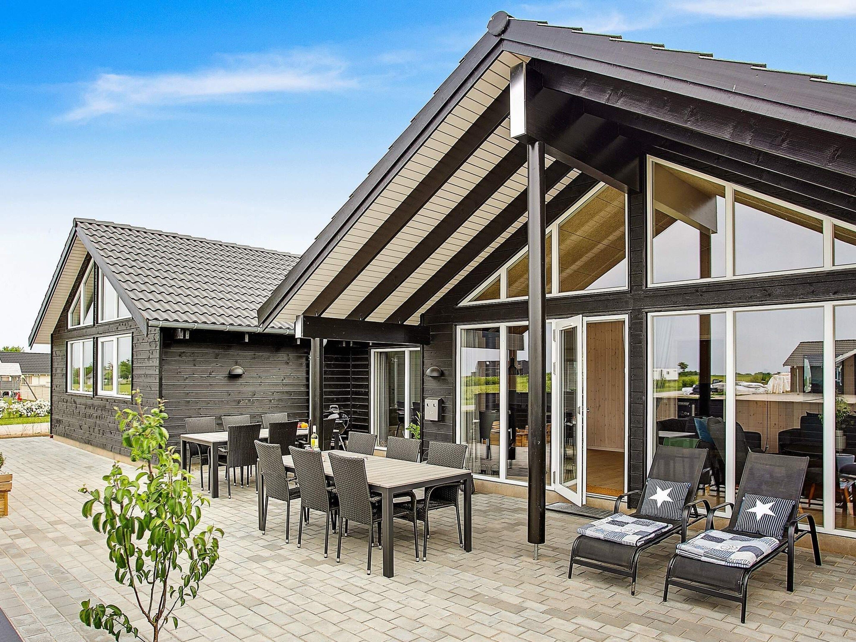 A modern house with a patio area featuring a dining table and chairs, a small garden, and a large windowed porch.