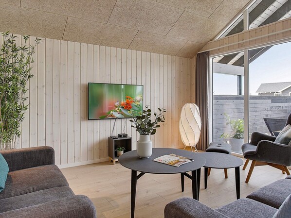 A modern living room with a flat-screen TV, a round coffee table, and grey sofas.