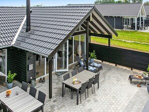 Eine moderne Außenpatio mit Essbereich, einer überdachten Sitzgruppe und Blick auf eine Wiese.