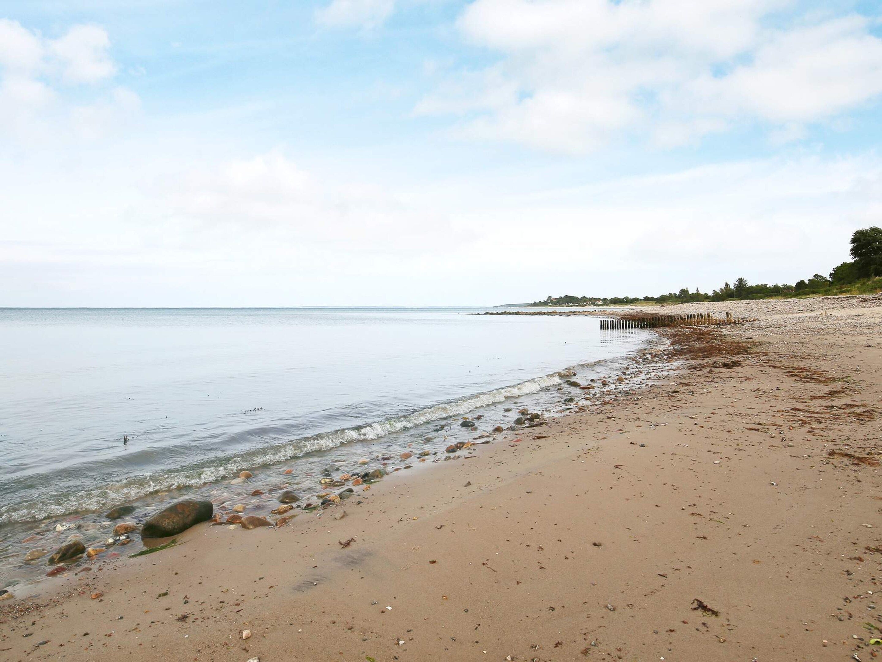 A beach with a wooden pier extending into calm waters, surrounded by a clear sky.