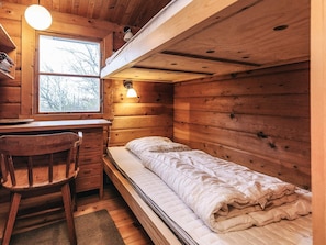 Quarto compacto estilo cabine com beliche, escrivaninha com cadeira e janela com vista para árvores.