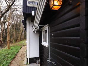 A black wooden building with a white window and a door, a small window, and a metal railing.