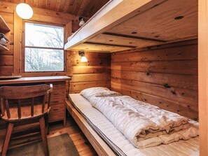 A compact cabin-style room with a bunk bed, a desk with a chair, and a window providing a view of the outdoors.
