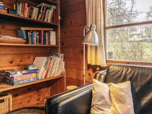 A cozy cabin interior with wooden walls, a bookshelf filled with books, a desk with a lamp, and a window with a view of trees. - 6 Person Holiday Home in Dronningmolle-by Traum (Dronningmolle)