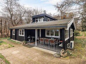 A cabin with a covered patio, a barbecue grill, and a small outdoor seating area.