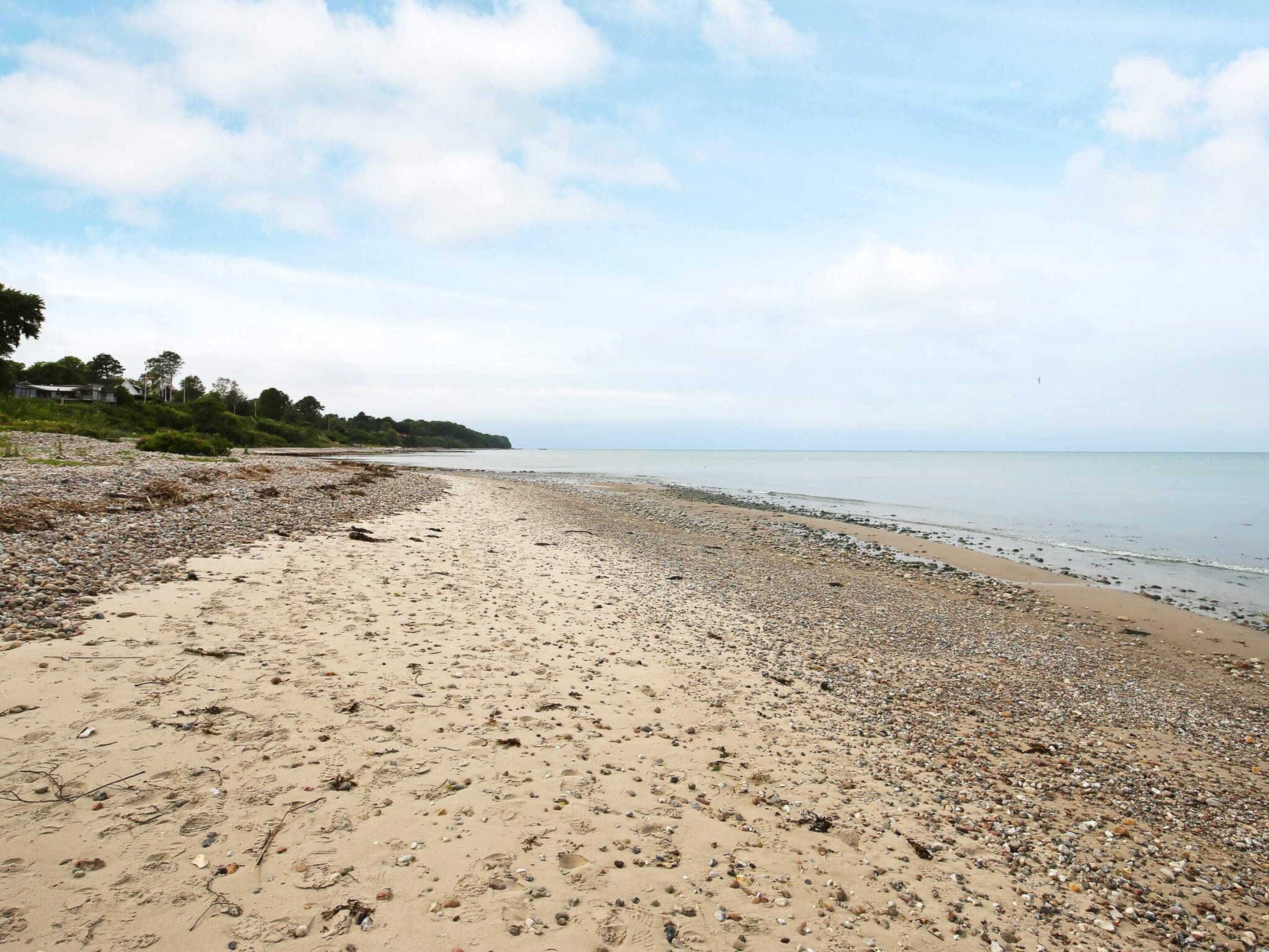 A beach with pebbles and sand, a clear sky, and a calm sea.