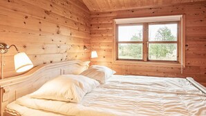 A wooden cabin bedroom with a bed, two bedside lamps, and a window with a view of trees. - 5 Person Holiday Home in Strandby-by Traum (Strandby)